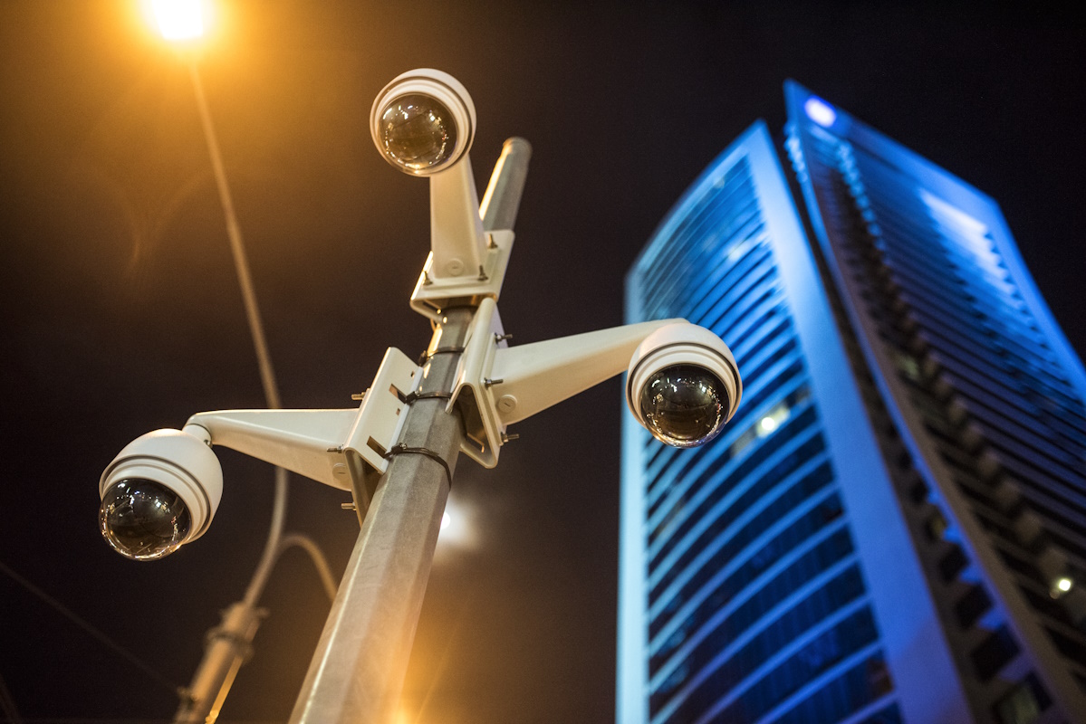 Cluster of modern dome security cameras mounted on a pole in an urban setting at night, with a tall illuminated building and streetlight in the background.